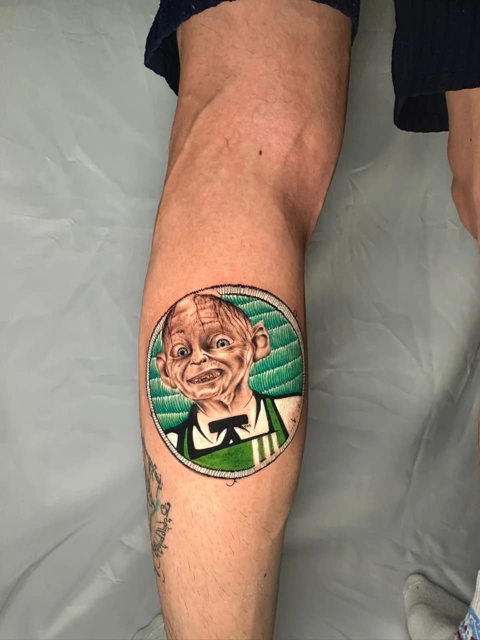 Baldırda yeşil zemin üzerinde yuvarlak çerçeveli renkli Gollum portresi